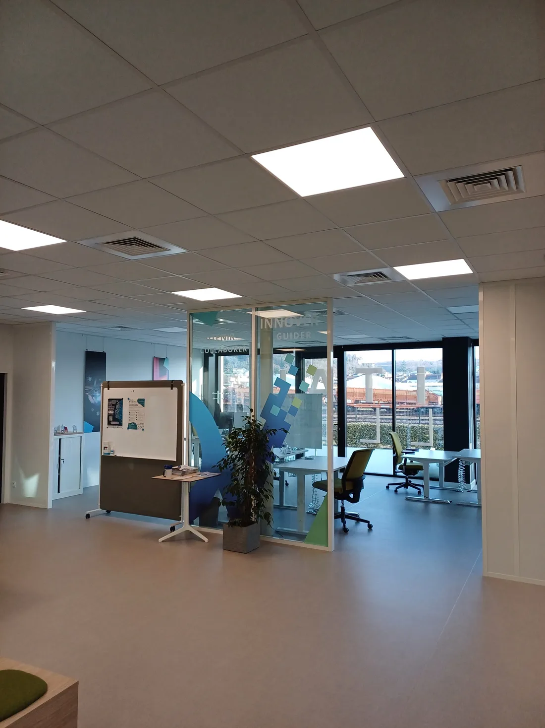 Bureaux de Digital Valley derrière une cloison vitrée, avec vue sur les voies ferrées.